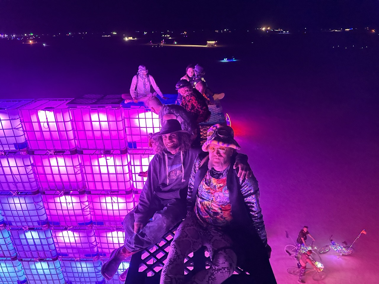 Nighttime portrait of camp members sitting on a glowing elevated structure.